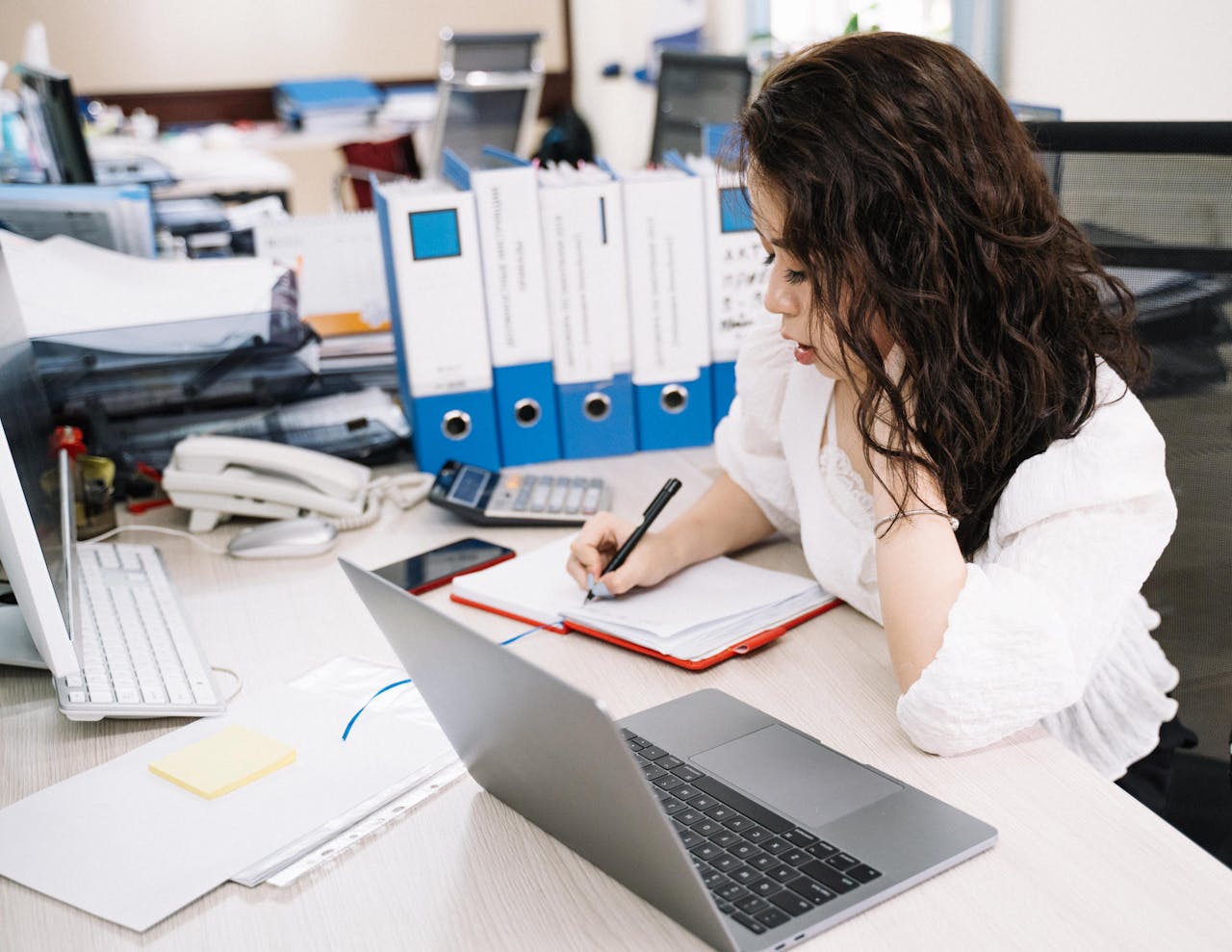 award-img An office worker takes notes while working at a desk with a laptop and documents.